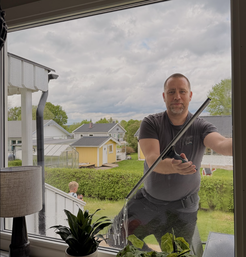 Kristopher putsar ett fönster inifrån med barn i bakgrunden
