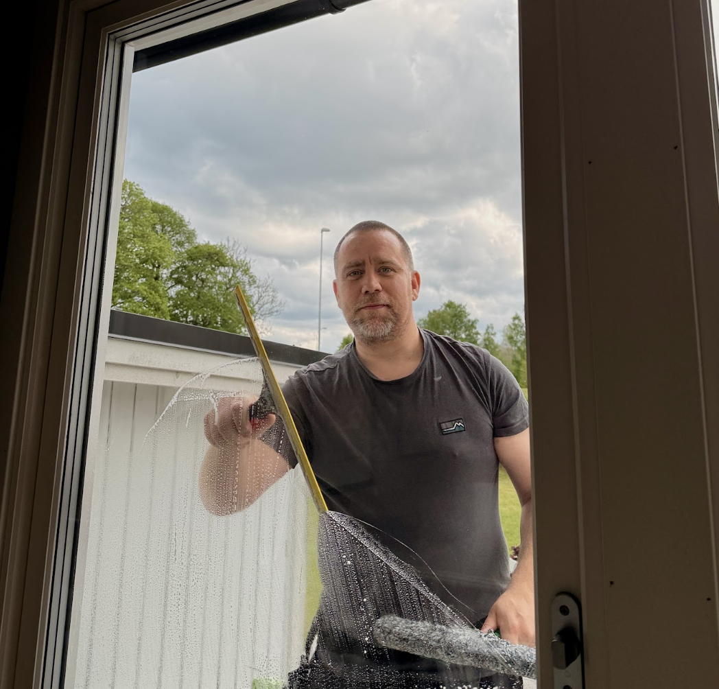 Kristopher putsar ett fönster hos en kund i Marbäck